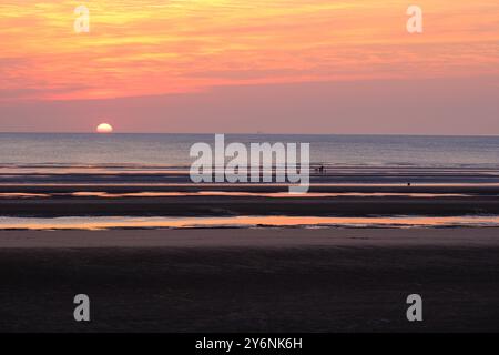 Ruhiger Sonnenuntergang über einem Strand mit exponierten Wattflächen und entferntem Horizont. Stockfoto