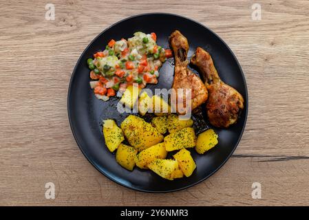 Zwei gebratene Hähnchenstangen auf einem Teller mit Kartoffeln und gekochtem Gemüse. Stockfoto