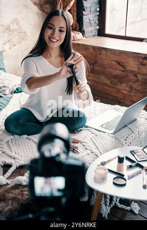 Ratschläge geben. Draufsicht über die schöne junge Frau, die Makeup Pinsel hält und lächelt, während sie Social Media-Videos macht Stockfoto