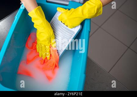 Ein Paar Hände mit gelben Gummihandschuhen, die ein Tuch gegen ein graues Waschbrett schrubben. Die traditionelle Methode des Händewaschens ist effektiv zum Entfernen Stockfoto