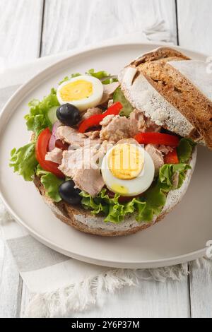 Pan Bagnat ist ein Sandwich mit Salat Nicoise, bestehend aus rohem Gemüse, hart gekochten Eiern, Sardellen und Thunfisch aus der Nähe auf dem Teller auf dem Holztisch. Stockfoto