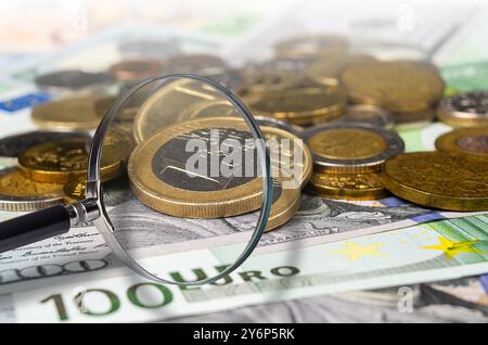 Detaillierte Darstellung verschiedener internationaler Währungen und Münzen unter einer Lupe als Symbol für Finanzanalysen und Konzepte der Weltwirtschaft. Stockfoto
