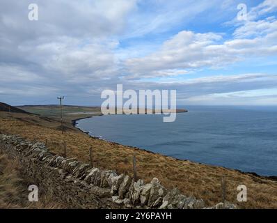 Eine Küstenlandschaft mit einer Steinmauer und grasbewachsenen Hügeln mit Blick auf das Meer unter teilweise bewölktem Himmel. Stockfoto