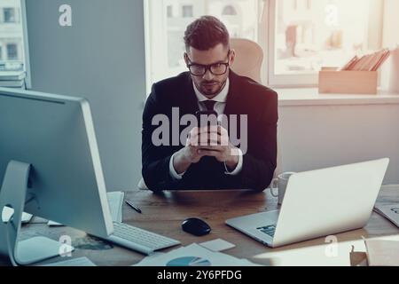 Immer verfügbar. Hübscher junger Mann in formaler Kleidung, der sein Smartphone benutzt, während er im Büro sitzt Stockfoto