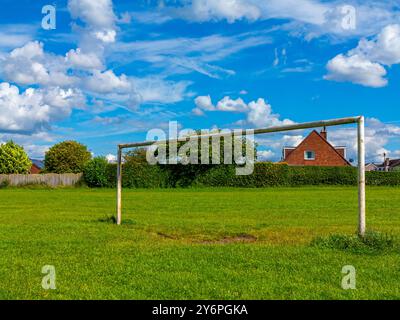 Torpfosten auf einem Fußball- oder Fußballfeld in einem Vorstadtpark mit Häusern dahinter und blauem Himmel mit weißen Wolken darüber. Stockfoto