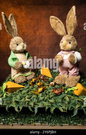 Zwei gefüllte Kaninchen sitzen auf einem grünen Teppich mit Karotten und Schokolade vor ihnen Stockfoto