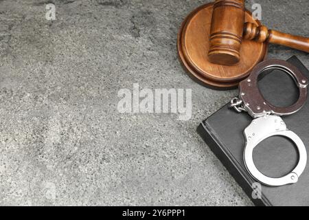 Buch, richterlicher Hammer und Handschellen auf grauem, strukturiertem Tisch, über der Ansicht. Leerzeichen für Text Stockfoto