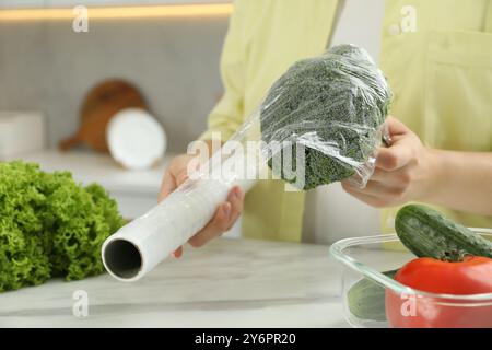 Frau, die Plastikfolie über Brokkoli auf der Arbeitsplatte in der Küche legt, Nahaufnahme Stockfoto