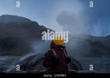 Ein Wanderer in gelber Mütze und violetter Jacke steht in der Nähe von Tatio Geysers. San Pedro de Atacama, Chile Stockfoto