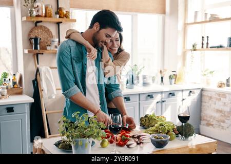 Gemacht, um einander zu lieben. Wunderschönes junges Paar, das Abendessen kocht, während es zu Hause in der Küche steht Stockfoto