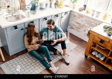 Liebe ist alles, was zählt. Blick von oben auf das schöne junge Paar, das Wein trinkt, während es zu Hause auf dem Küchenboden sitzt Stockfoto