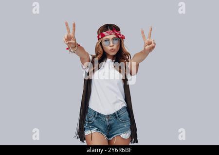 Attraktive, stilvolle junge Frau, die vor grauem Hintergrund in die Kamera blickt und puckert Stockfoto