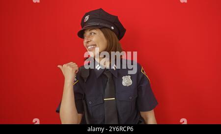 hispanische Polizistin mittleren Alters lächelt und gibt sich auf rotem Hintergrund zur Seite. Stockfoto