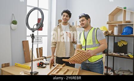 Zwei Männer arbeiten in einer hell beleuchteten Tischlerei zusammen, einer hält Holzstuhlteile und der andere positiv. Stockfoto