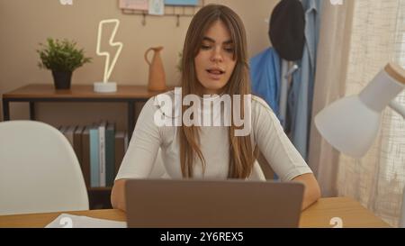 Fokussierte junge Frau mit Laptop in gemütlichem Heimbüro, mit moderner Einrichtung und Zimmerpflanzen Stockfoto