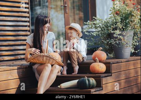 Eine Frau und ein Kind sitzen auf Holztreppen mit Kürbissen und einem Korb und genießen einen sonnigen Tag draußen. Stockfoto