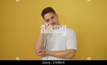 Ein nachdenklicher junger hispanischer Mann mit einem ordentlichen Bart posiert vor einem glatten gelben Hintergrund und strahlt ungezwungenes Selbstvertrauen aus. Stockfoto