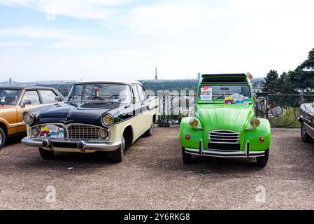 Ein Simca Chambord und ein hellgrüner Citroën 2CV auf einer Open-Air-Ausstellung in der Nähe von Paris. Im Hintergrund der Blick auf Paris und den Eiffelturm Stockfoto