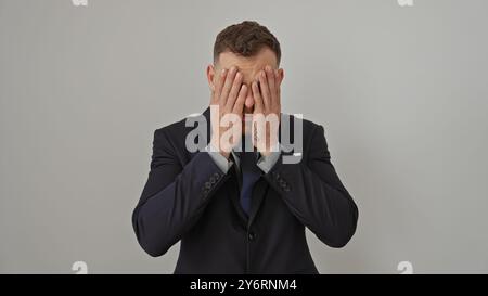 Ein gestresster Geschäftsmann bedeckt sein Gesicht mit den Händen, trägt einen Anzug vor weißem Hintergrund. Stockfoto