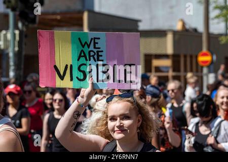 Wir sind sichtbar. Junge Frau mit einem handgefertigten Schild bei der Helsinki Pride 2024 Parade auf der Mannerheimintie in Helsinki, Finnland. Stockfoto