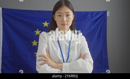 Eine zuversichtliche asiatin steht in einem Innenbereich vor einer Flagge der europäischen union. Stockfoto