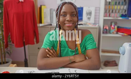 Porträt einer selbstbewussten afrikanerin mit Zöpfen, grünem Kleid und Maßband in einer Schneiderei. Stockfoto