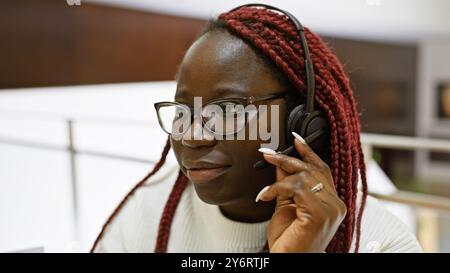 Eine professionelle afrikanische Frau mit Zöpfen, die ein Headset in einem Büro verwendet, stellt ein Porträt des modernen Arbeitsplatzes dar. Stockfoto