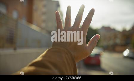 Die Hand des Mannes streckt in einer urbanen Umgebung zur Sonne, mit verschwommenen Autos und Gebäuden im Hintergrund. Stockfoto