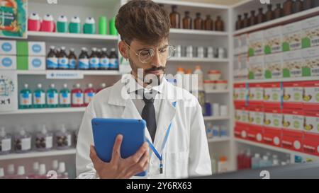 Schöner hispanischer Apotheker mit Bart, der Tablette in einer modernen Drogerie verwendet Stockfoto