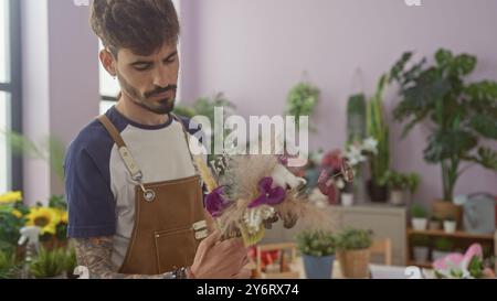 Ein tätowierter junger Mann arrangiert aufmerksam einen Blumenstrauß in einem Blumenladen voller Pflanzen. Stockfoto