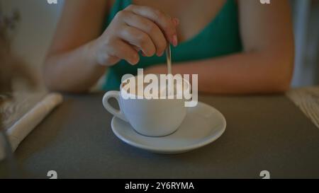 Eine junge hispanische Frau genießt drinnen einen Kaffee in einer Cafeteria in italien und rührt ihr Getränk mit einem Löffel um. Stockfoto