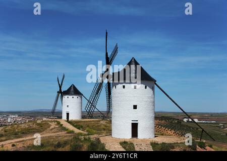 Zwei weiße Windmühlen auf einem Hügel mit Blick auf eine weite Landschaft unter blauem Himmel an einem sonnigen Tag, Alcazar de San Juan, Ciudad Real, Castilla-La Mancha, Rout Stockfoto