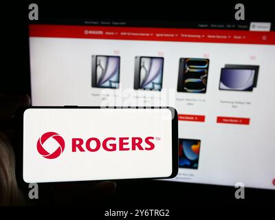 In dieser Abbildung hält eine Person ein Smartphone mit dem Logo des kanadischen Kommunikationsunternehmens Rogers Communications Inc. Vor der Website. Stockfoto