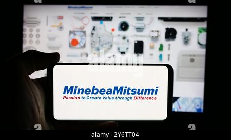 In dieser Abbildung hält eine Person ein Mobiltelefon mit dem Logo des japanischen Elektronikunternehmens MinebeaMitsumi Inc. Vor der Webseite. Stockfoto