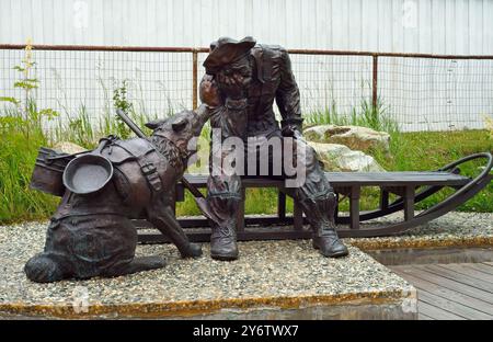 Auf einem kleinen Grundstück in Skagway, Alaska, befindet sich eine Bronzestatue eines übermüdeten Goldsuchers und seines treuen Schlittenhundes. Stockfoto