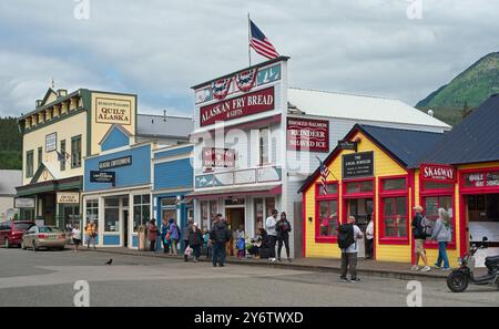 An einem bewölkten Sommermorgen in Skagway, Alaska, gibt es eine Reihe von Touristenläden und Attraktionen, die einen Block der Broadway Avenue füllen. Stockfoto