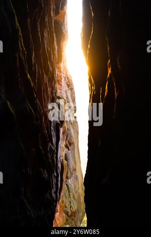 Goldenes Sonnenlicht filtert im Herbst durch eine schmale Spalte in Sandsteinfelsen, die ein warmes Leuchten erzeugt und die reichhaltigen Strukturen der Felsformationen in der Dämmerung verstärkt. Stockfoto