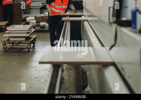 Zwei fleißige Arbeiter in hellen reflektierenden Westen manövrieren große Materialplatten und sorgen so für reibungslose Arbeitsabläufe in einer gut beleuchteten Werkstatt, umgeben von oder Stockfoto