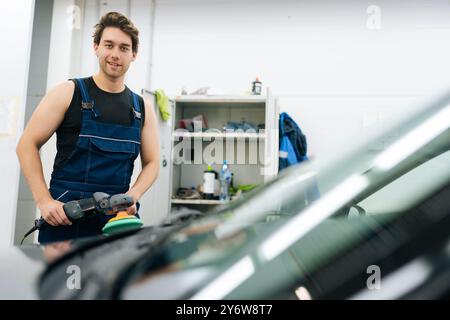 Porträt eines gutaussehenden Autoarbeiters mit muskulöser Karosserie Polierwagen in der Autowerkstatt mit Orbitalpolierer, lächelnd in die Kamera blickend. Stockfoto