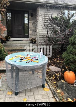 Halloween-Leckereien und Handdesinfektionsmittel stehen auf einem Tisch vor dem Haus, sodass Kinder unter Wahrung sozialer Distanz „Trick-or-Treat“-Effekte genießen können. Stockfoto