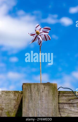 Ein buntes Windrad auf einem Holzpfosten vor einem hellblauen Himmel mit verstreuten Wolken. Stockfoto