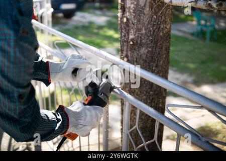 Nahaufnahme eines Arbeiters, der mit einem Winkelschleifer einen Metallzaun schneidet Stockfoto