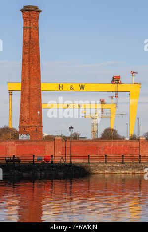 Alter Industrieschornstein am Ufer des Flusses Lagan und gelbe Kräne in Belfast Harland & Wolff Werft im Hintergrund. Stockfoto