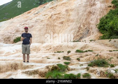 Der Entdecker navigiert fremdes Gelände, Smartphone in der Hand, zwischen goldenen Kalziumablagerungen und karger Vegetation. Stockfoto