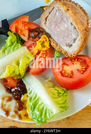 Mit Salat arrangiert, auf einem hölzernen Schneidebrett mit losen Gebäckbröseln, auch Salat und in Olivenöl geschnittene Tomaten im Hintergrund. Stockfoto