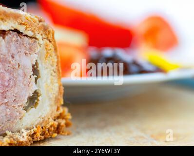 Abstrakter Blick auf einen leckeren traditionellen britischen Snack zur Mittagszeit in mittlerer Zubereitung, auf einem hölzernen Schneidebrett, mit süßer Gurke, Senf und Tomaten als A Stockfoto