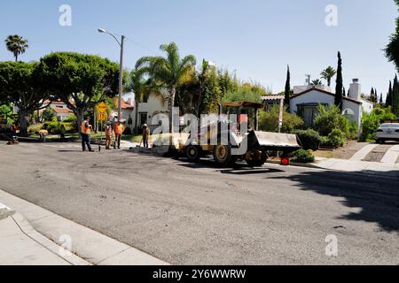 Die Straße wird erneuert, wobei Arbeiter und Maschinen aktiv am Prozess beteiligt sind. Zur Ausstattung gehören ein Planierschild und ein Kipplader. Stockfoto