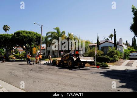 Die Straße wird erneuert, wobei Arbeiter und Maschinen aktiv am Prozess beteiligt sind. Zur Ausstattung gehören ein Planierschild und ein Kipplader. Stockfoto