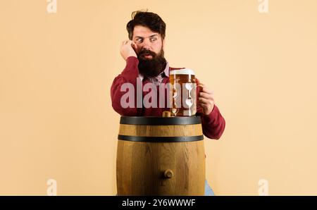 Ein überraschter bärtiger Mann trinkt köstliches Bier im Pub oder in der Bar. Craft-Bier im Restaurant. Deutschland Tradition. Holzfässer und ein Glas Bier. Gut Aussehend Stockfoto