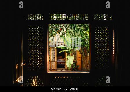 Ruhiger Blick durch das Fenster auf den üppigen botanischen Innenhof in einem Riad in Marrakesch, traditionelle marokkanische Architektur mit tropischem Grün, Unterkunft, Stockfoto